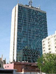 Tower with blue glass facade and white concrete sides, and a framed communication mast at the top